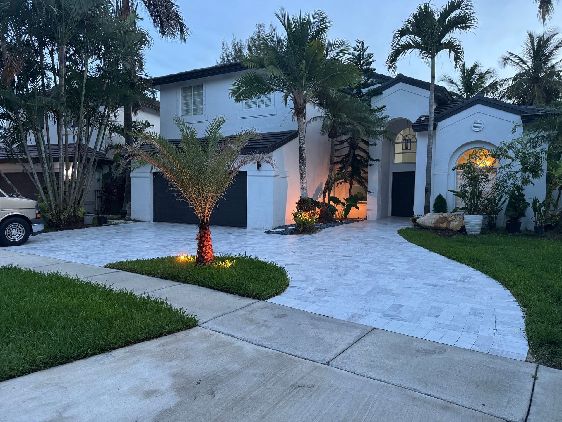 Modern house with palm trees, illuminated driveway, and an arched entrance at dusk.